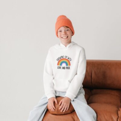 Ett barn som har en vit tröja med regnbågstryck och texten "Growing up with love and pride".