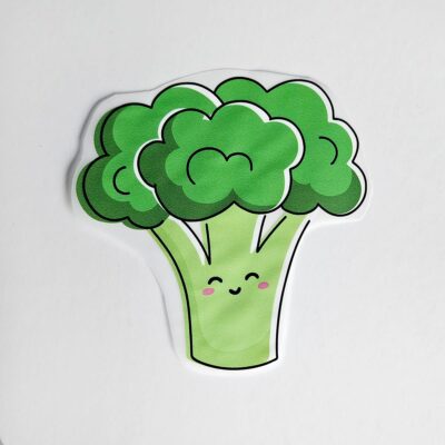 Textiltryck med en grön broccoli med ansikte och rosa kinder.
