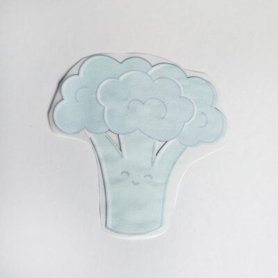Baksidan av textiltryck med en grön broccoli med ansikte och rosa kinder.
