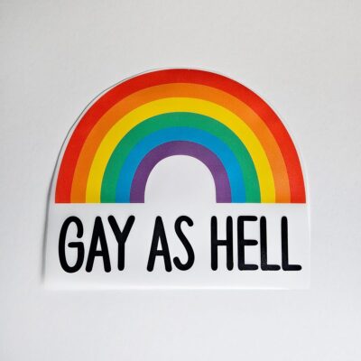 Regnbåge i flera färger med texten ”GAY AS HELL”.